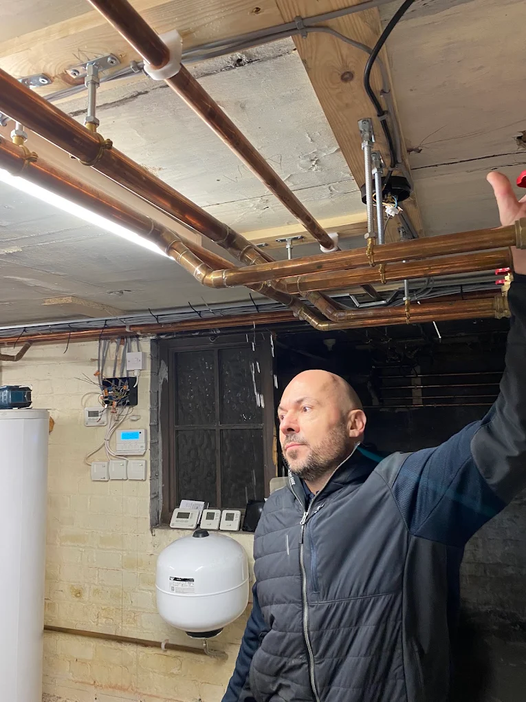 Copper pipework and hot water cylinder installation run neatly across a basement ceiling